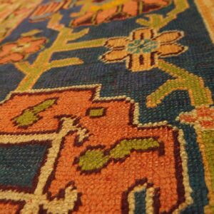 Low pile rug texture with stepped geometric and floral designs in orange, blue, green, and gold.