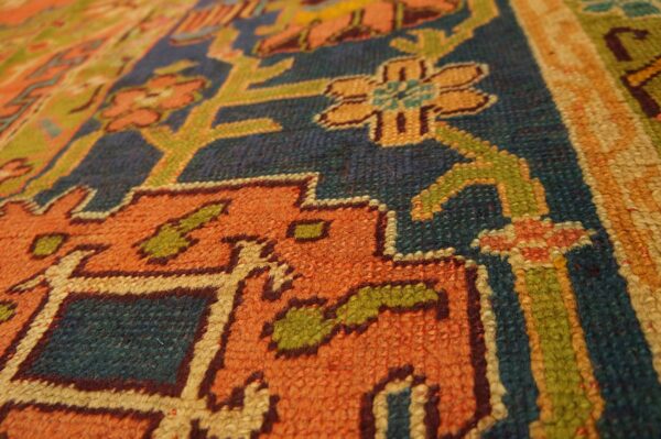 Low pile rug texture with stepped geometric and floral designs in orange, blue, green, and gold.