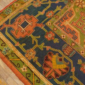 Geometric rug in navy, coral, and lime green with stylized patterns rests on light wood planks.