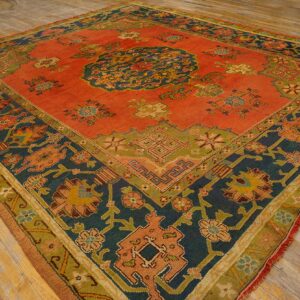 Low-pile rust and navy patterned rug with green accents and fringe laying on light wooden floorboards.