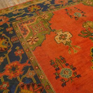 Rust orange patterned rug with stepped navy and moss green borders and geometric motifs on a wood floor.