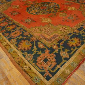 Low-pile rug with a rust-orange field and geometric floral patterns in navy, olive, and gold on wood flooring.