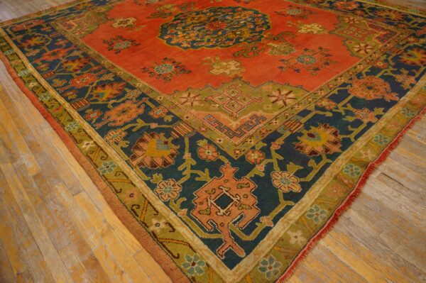 Low-pile rug with a rust-orange field and geometric floral patterns in navy, olive, and gold on wood flooring.