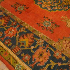 Rust rug with dark blue and green borders and geometric patterns, shown on light hardwood floors.