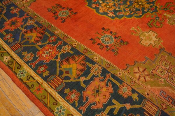 Rust rug with dark blue and green borders and geometric patterns, shown on light hardwood floors.