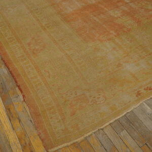 Low-pile rug in faded yellow and rust geometric patterns displayed on worn wooden flooring.