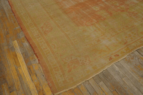 Low-pile rug in faded yellow and rust geometric patterns displayed on worn wooden flooring.