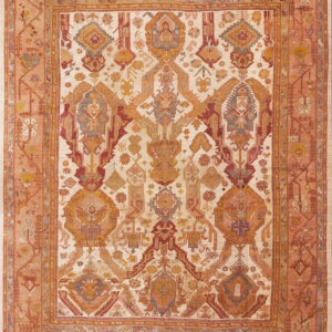A detailed, high-pile rug with geometric motifs in rust, gold, and blue on a pale cream ground.