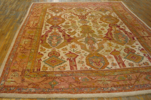 Large area rug with a cream field and tribal patterns in rust, gold, and teal, resting on wood floorboards.