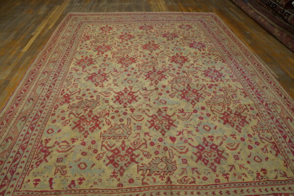 Textured yellow rug with a complex, pixelated pattern in faded red and slate blue on wood planks.