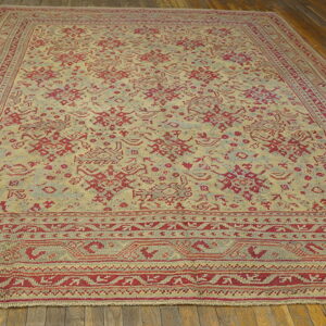 Large area rug with red geometric patterns on a beige field rests on distressed hardwood floors.