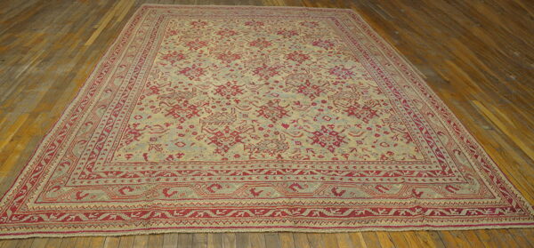 Large area rug with red geometric patterns on a beige field rests on distressed hardwood floors.