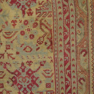 Textured yellow rug featuring complex red and sage geometric motifs and a wide border on wood planks.