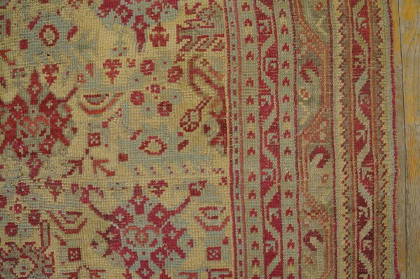 Textured yellow rug featuring complex red and sage geometric motifs and a wide border on wood planks.