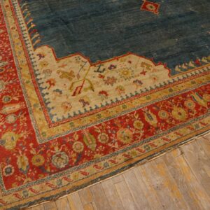 Worn blue rug with red and gold layered border on distressed wide-plank wooden flooring.