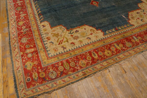 Worn blue rug with red and gold layered border on distressed wide-plank wooden flooring.