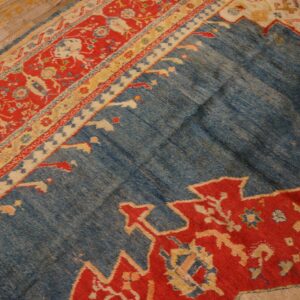 Blue rug detail showing abrash texture, red geometric motifs, and ornate borders on wooden flooring.