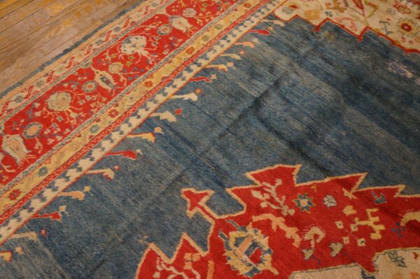 Blue rug detail showing abrash texture, red geometric motifs, and ornate borders on wooden flooring.