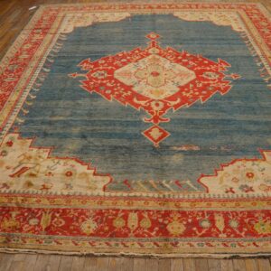 Distressed blue rug with a large red and cream geometric medallion on wide wood plank flooring.