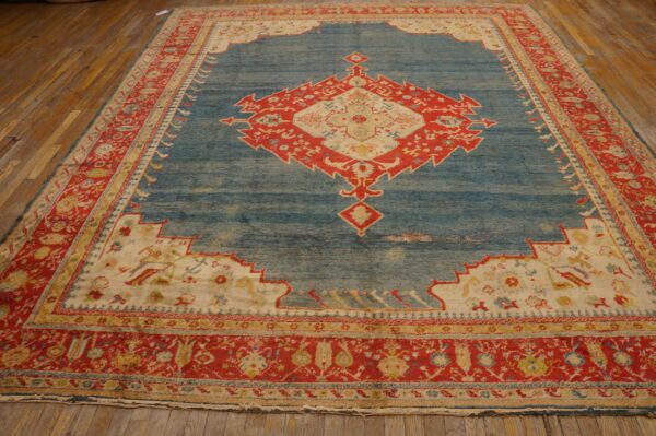 Distressed blue rug with a large red and cream geometric medallion on wide wood plank flooring.