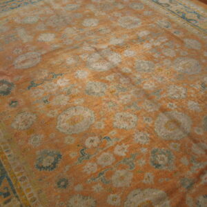 Distressed area rug in faded orange with large floral medallions patterned in gray and dusty blue.