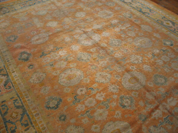 Distressed area rug in faded orange with large floral medallions patterned in gray and dusty blue.