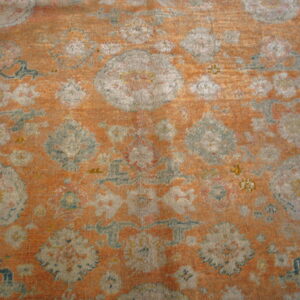 Textured rug detail showing large, faded gray and sage floral designs on an apricot orange field.