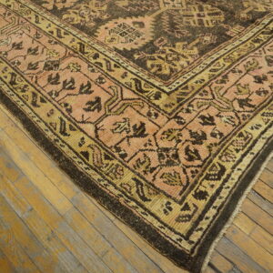A patterned low-pile rug in dark brown, peach, and gold rests on distressed wood flooring.