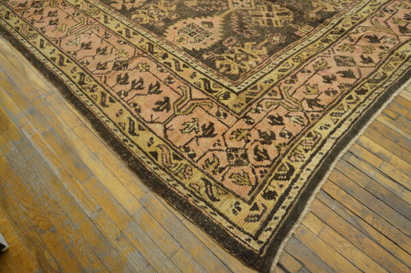 A patterned low-pile rug in dark brown, peach, and gold rests on distressed wood flooring.