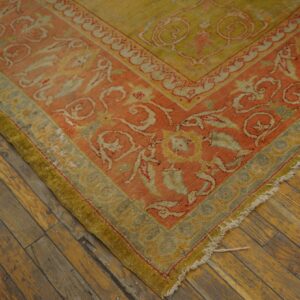 Low-pile rug in coral, moss green, and yellow patterns rests on rustic hardwood flooring.
