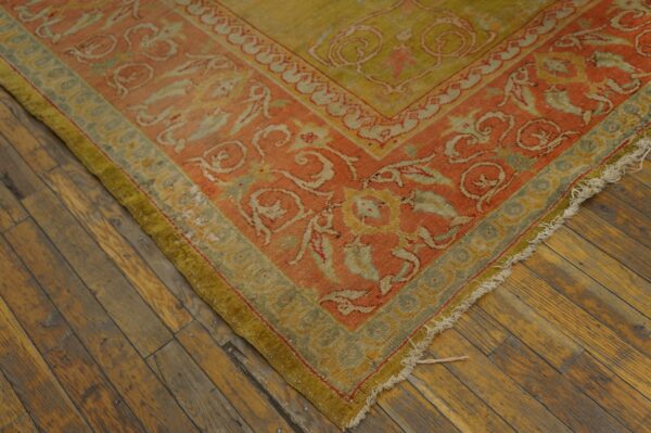 Low-pile rug in coral, moss green, and yellow patterns rests on rustic hardwood flooring.