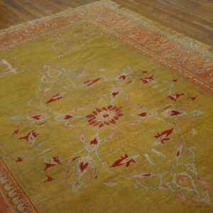 Faded chartreuse rug with red and peach floral patterns and a wide border on brown hardwood flooring.