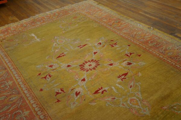 Faded chartreuse rug with red and peach floral patterns and a wide border on brown hardwood flooring.