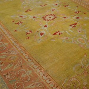 Muted yellow-green rug featuring a red and coral floral medallion and a wide patterned border on wood floor.