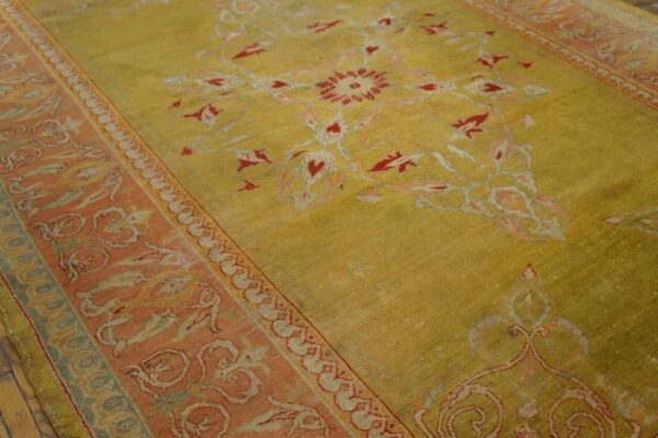 Muted yellow-green rug featuring a red and coral floral medallion and a wide patterned border on wood floor.