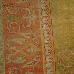 Muted rust and sage green patterned borders meet a textured, olive gold central field on wood flooring.