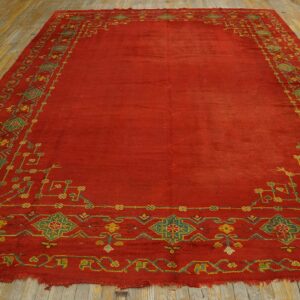 Low-pile red rug with green and yellow geometric borders on worn wooden planks.