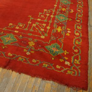 Red rug with high pile and complex geometric patterns in teal and yellow on distressed wood flooring.