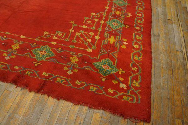 Red rug with high pile and complex geometric patterns in teal and yellow on distressed wood flooring.