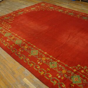 A large red rug with geometric yellow and green borders rests on worn wooden floors.