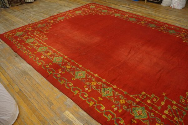 A large red rug with geometric yellow and green borders rests on worn wooden floors.