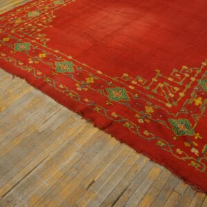 Red rug with intricate yellow and teal patterned borders rests on rustic wood flooring.