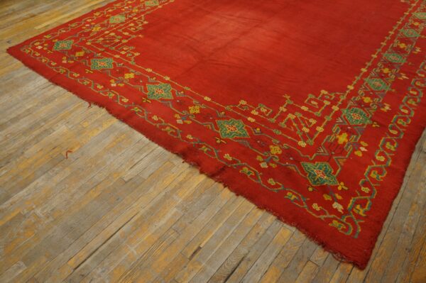 Red rug with intricate yellow and teal patterned borders rests on rustic wood flooring.