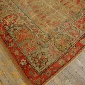 Distressed rug corner with rust, tan, and sage traditional motifs rests on worn wooden floorboards.