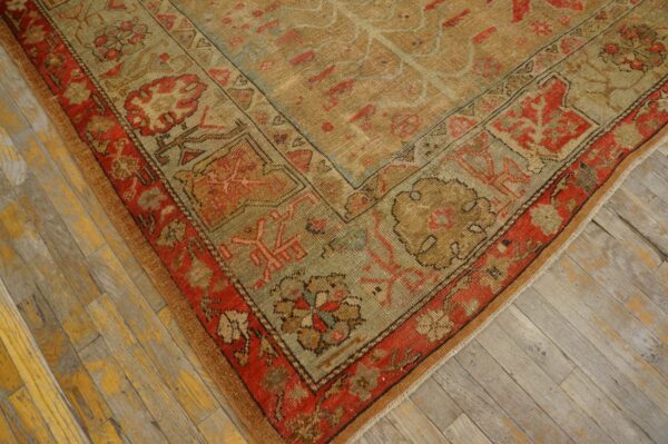 Distressed rug corner with rust, tan, and sage traditional motifs rests on worn wooden floorboards.