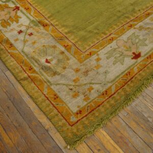 Olive green high-pile rug with floral gold and cream border rests on rustic hardwood flooring.