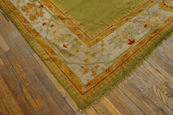 Olive green high-pile rug with floral gold and cream border rests on rustic hardwood flooring.