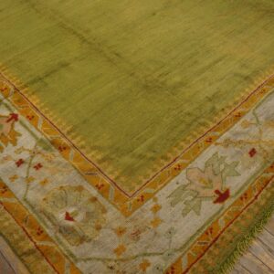 Low pile green rug with thick floral border in mustard, cream, and red on distressed wooden floors.