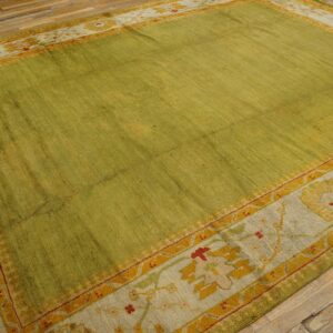 A textured green rug with a patterned border in yellow, red, and pale taupe rests on wide plank wood floor.