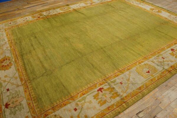 A textured green rug with a patterned border in yellow, red, and pale taupe rests on wide plank wood floor.